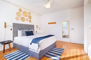 Une chambre à coucher moderne avec un lit, des tables de chevet, une lampe fixée au mur, un miroir et un plancher en bois.