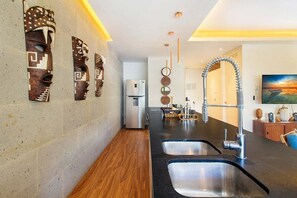 A modern kitchen with a stainless steel sink, a refrigerator, and decorative wall art. - 2BR Downtown Condo Walk to Coco Beach (Playa Del Carmen)