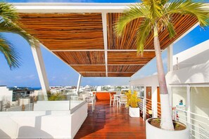 A modern rooftop terrace with a wooden ceiling, palm trees, and a view of the city. - 2BR Downtown Condo Walk to Coco Beach (Playa Del Carmen)