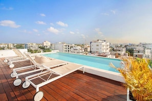 A rooftop pool with lounge chairs, surrounded by buildings. - 2BR Downtown Condo Walk to Coco Beach (Playa Del Carmen)