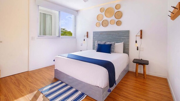 Une chambre moderne comprenant un lit, une fenêtre, un ventilateur de plafond, un luminaire fixé au mur et un élément décoratif mural.