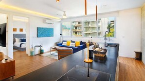 Une cuisine moderne avec un îlot central, un coin repas avec un canapé et une vue sur un immeuble d’habitation.