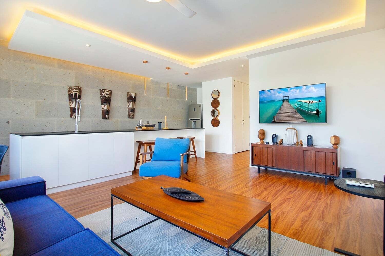 A modern living room with a wooden coffee table, blue sofa, and a large flat-screen TV mounted on the wall.