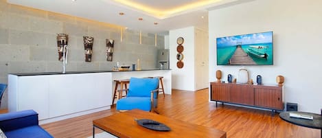 A modern living room with a wooden coffee table, blue sofa, and a large flat-screen TV mounted on the wall.