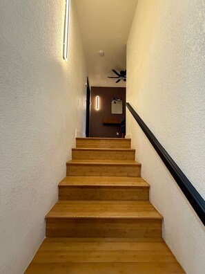 A wooden staircase with a black handrail leading to a room with a ceiling fan. - 5-Bedroom Luxury Home | Jacuzzi/Sauna/BBQ | 15 Min from the Strip (Las Vegas)