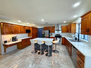 A modern kitchen with wooden cabinets, a central island with bar stools, and a stainless steel refrigerator. - 5-Bedroom Luxury Home | Jacuzzi/Sauna/BBQ | 15 Min from the Strip (Las Vegas)