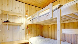 Habitación con literas, paredes de madera, un escritorio pequeño y una estantería.