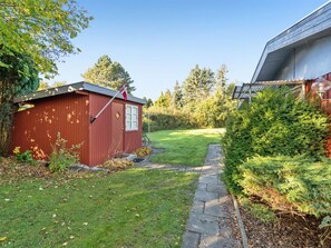 Ein roter Holzschuppen mit einer Flagge, ein gepflegter Rasen und ein Steinweg, der zu einem Haus mit Solaranlage führt.