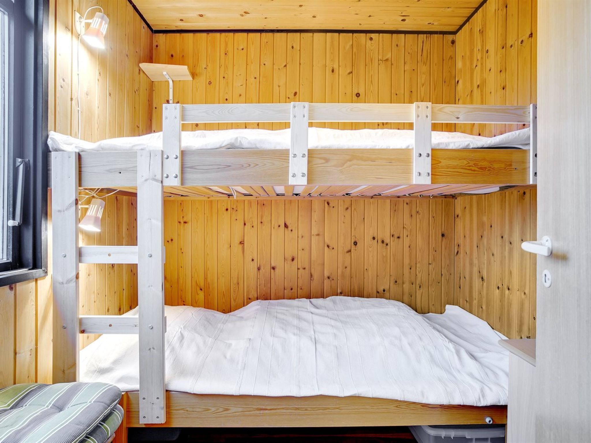 Een slaapkamer met stapelbed, houten wanden en een raam.