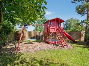 Une structure de jeu rouge avec un toboggan et une balançoire dans un jardin.