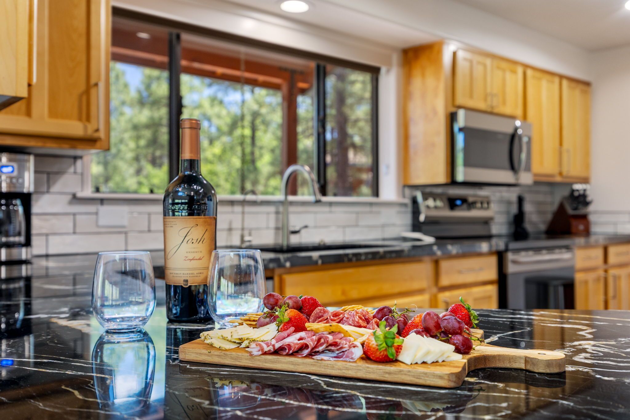 A kitchen with a marble countertop, a wine bottle, glasses, and a charcuterie board with meats and fruits.