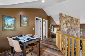 A dining area with a table set for four, a staircase with a wooden railing, and a stone wall. - RainbowLake-HotTub-GameRoom-Kayaks-Horseshoes-EVCharge-Firepit-Pickleball-7Beds (Pinetop-Lakeside)