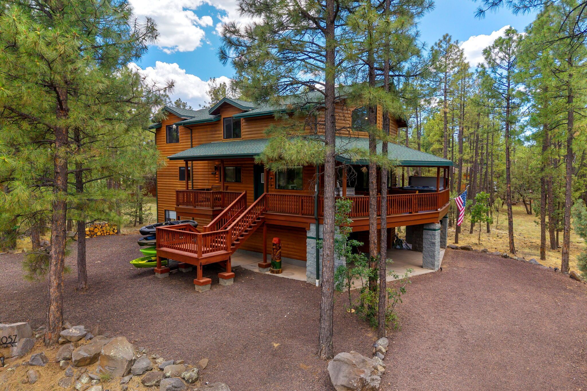 A two-story log cabin with a deck, surrounded by trees.