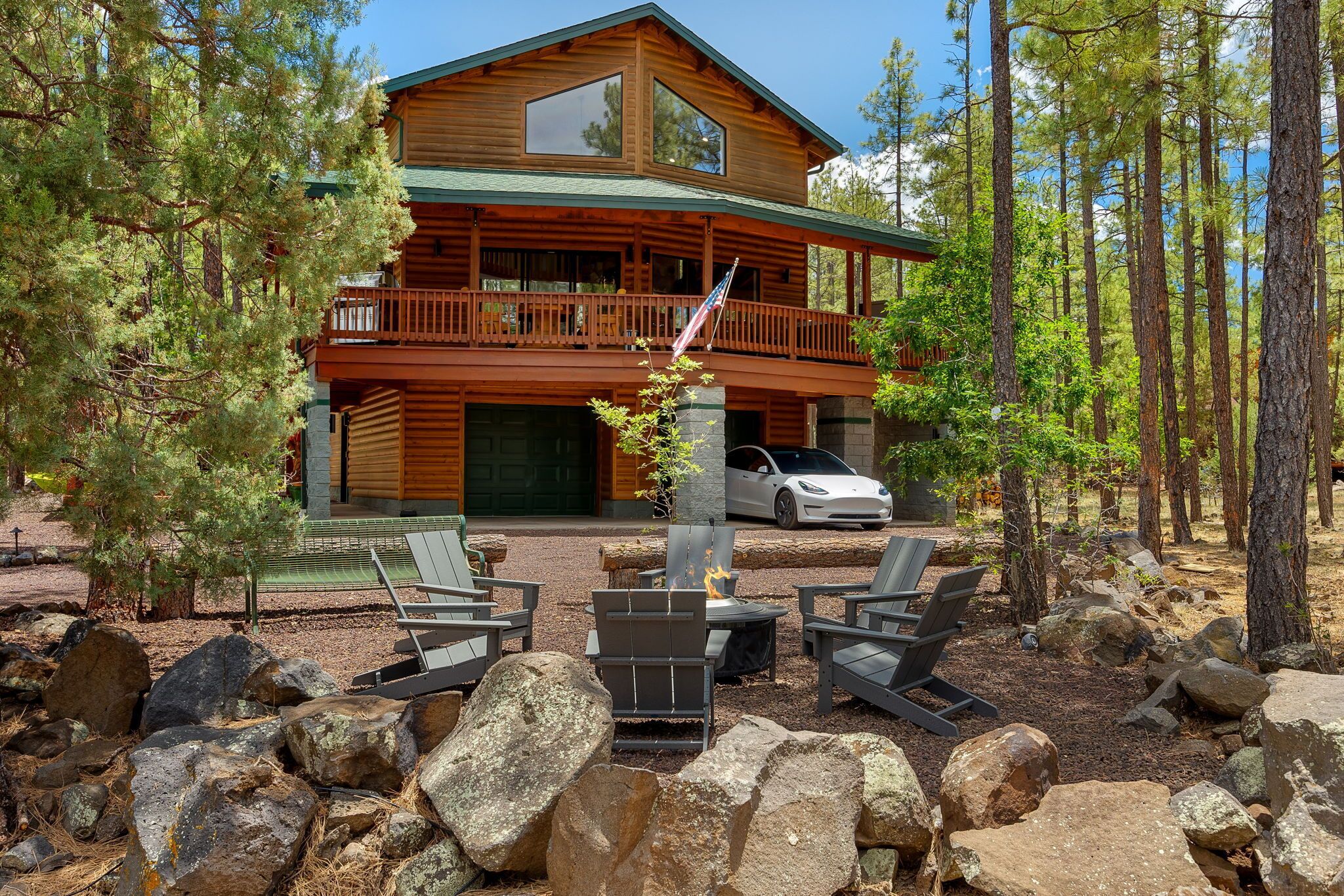 A two-story log cabin with a balcony, a stone fireplace, and a white car parked in front.