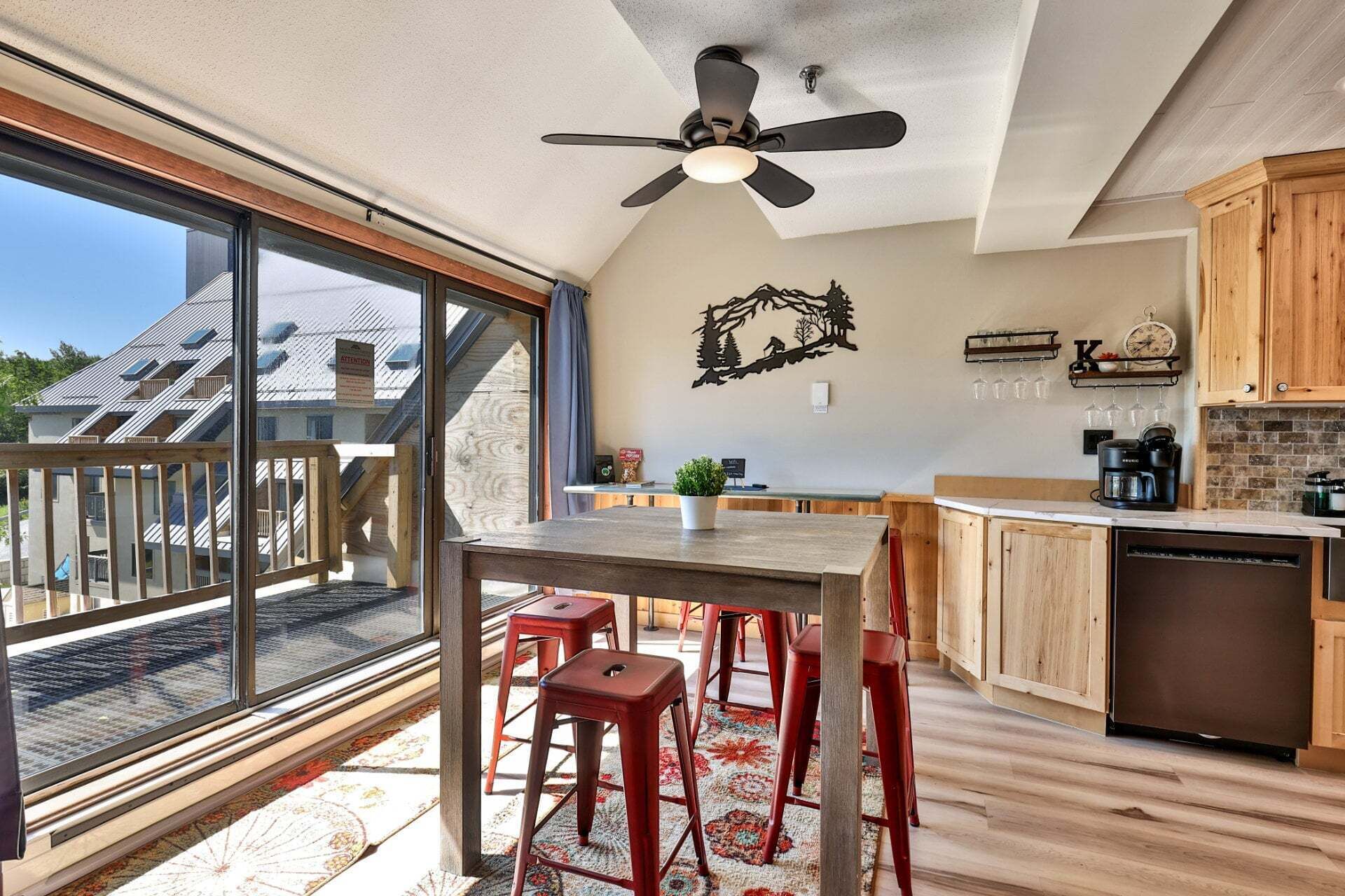 Une cuisine moderne avec un coin repas, de grandes fenêtres et une vue sur un immeuble d’habitation.