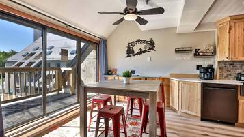 A modern kitchen with a dining area, large windows, and a view of a residential building.