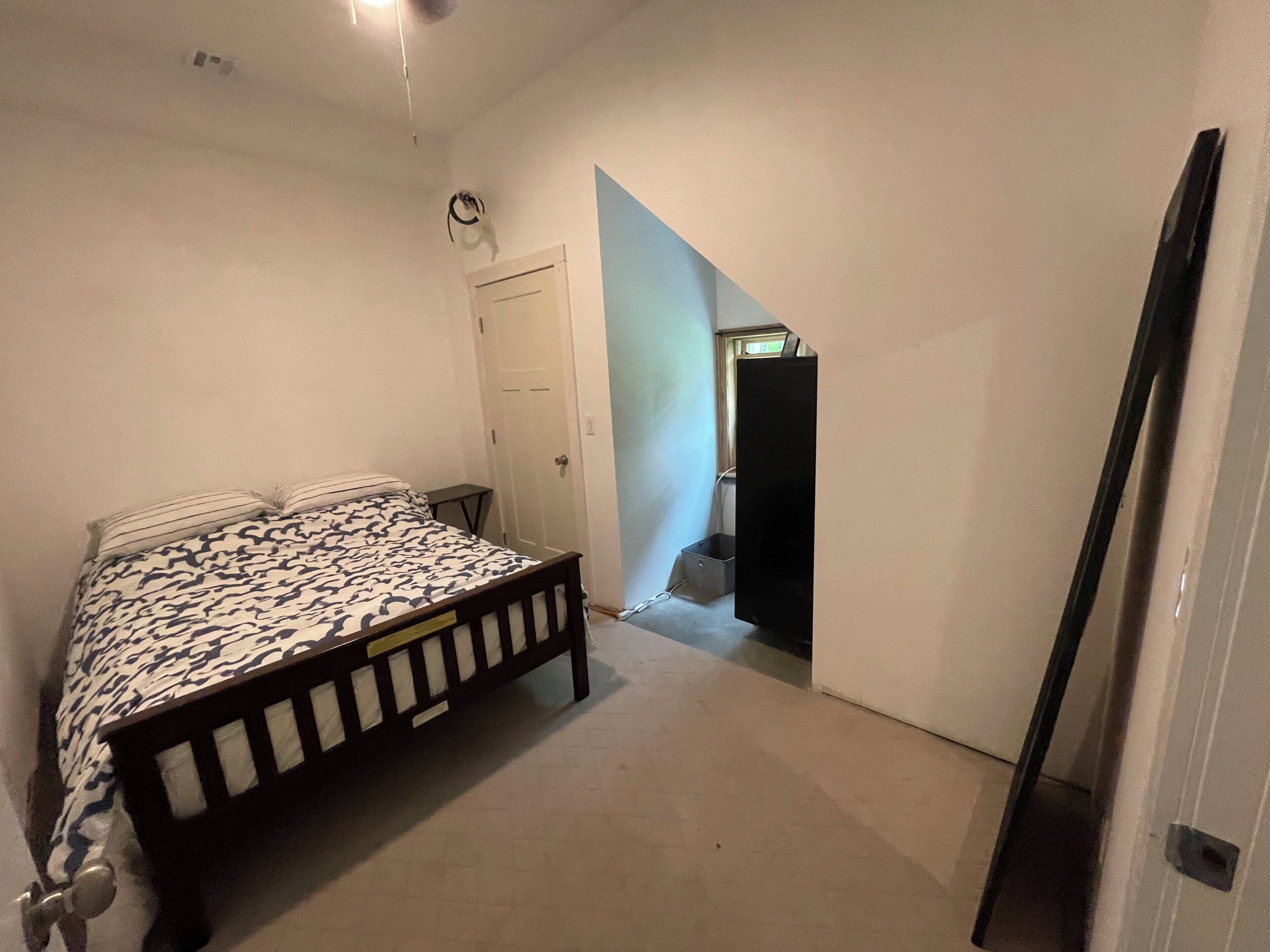 Quarto com cama, uma pequena mesa de cabeceira, uma porta e uma janela.