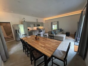 A modern kitchen with a built-in oven and microwave, a dining area with a wooden table and chairs, and a grey sofa in the living area. - Gardiner Forest Home on Awosting Preserve (Pine Bush)