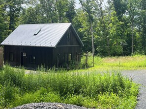 A rustic wooden barn with a metal roof, surrounded by dense greenery and trees. - Gardiner Forest Home on Awosting Preserve (Pine Bush)