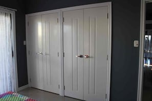 Una habitación con un armario amplio, una cama con una manta colorida y una ventana con cortinas.