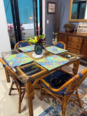 Ein Essbereich mit einem Glastisch, vier Holzstühlen mit blauen Kissen und einer Vase mit Blumen.
