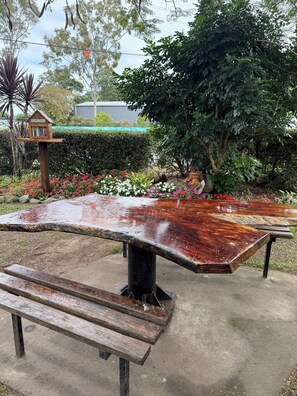 Una mesa de picnic con bancos, rodeada por un jardín con diversas plantas y flores.