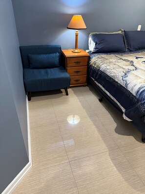 Ein Schlafzimmer mit einem Bett, einem Nachttisch, einer Lampe und einem blauen Sessel.