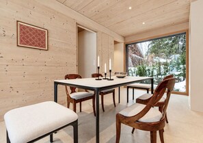 A dining area with a wooden table and chairs, a framed picture on the wall, and a window with a view of trees. - Historic Mazot Retreat by Mrs Miggins – Entire Chalet -Historic Mazot Retreat by Mrs Miggins offers (Lens)