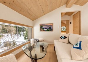 A modern interior with a glass table, white sofa, and a painting on the wall. - Historic Mazot Retreat by Mrs Miggins – Entire Chalet -Historic Mazot Retreat by Mrs Miggins offers (Lens)