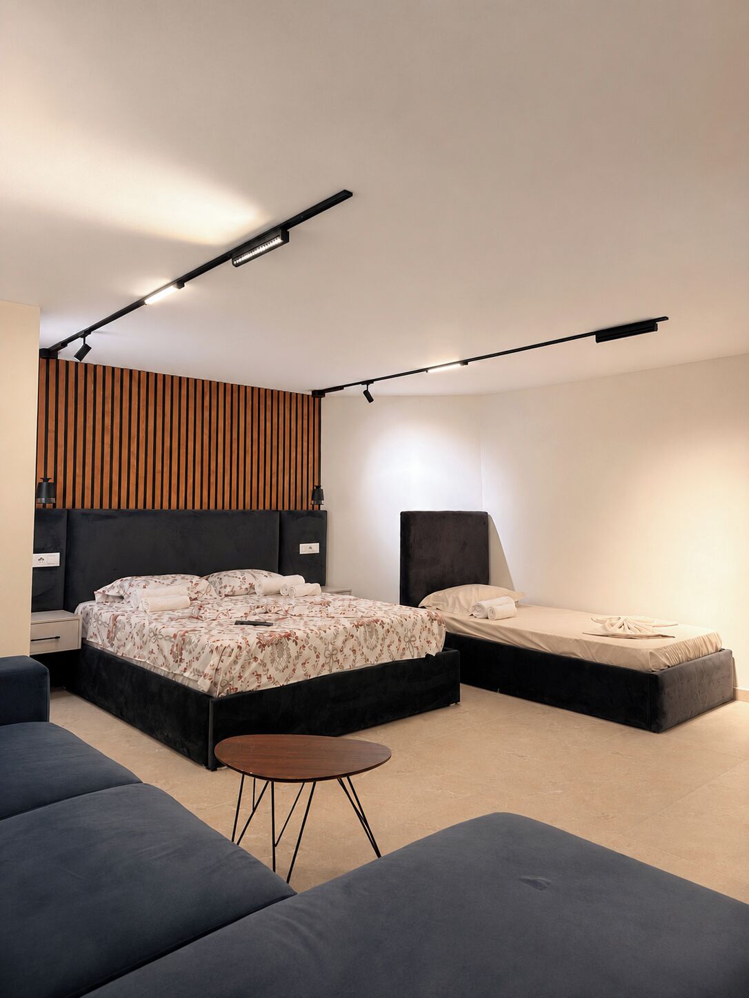 A modern bedroom with a large bed, a smaller bed, a sofa, and a small table.