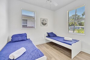 Une chambre avec deux lits, un ventilateur de plafond et une fenêtre avec des stores.