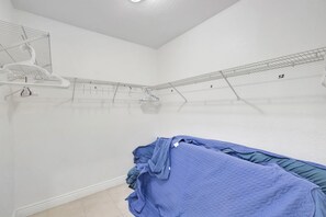 Une pièce avec un lit, un étendoir à linge en métal et un mur blanc.