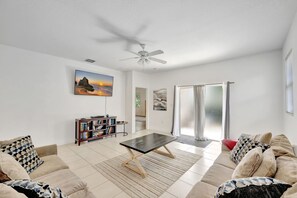 Un salon spacieux doté d’un ventilateur de plafond, d’un ensemble de canapés, d’une table basse et d’une bibliothèque.