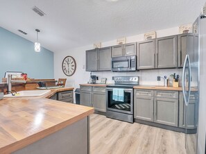 A modern kitchen with grey cabinets, stainless steel appliances, a wooden countertop, and a wall clock. - Charming 4-bedroom house with AC in welcoming Davenport (Davenport)