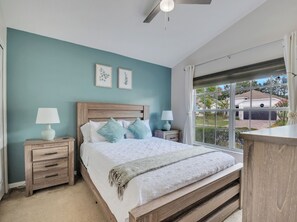 A bedroom with a bed, two bedside tables, a ceiling fan, and a window with a view of a house. - Charming 4-bedroom house with AC in welcoming Davenport (Davenport)