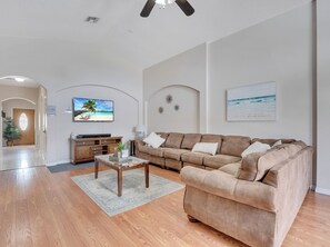A spacious living room with a large brown sectional sofa, a coffee table, and a flat-screen TV mounted on the wall. - Charming 4-bedroom house with AC in welcoming Davenport (Davenport)