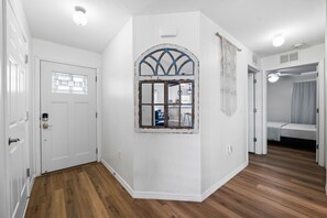A room with a white door, a window with a decorative frame, wooden flooring, and a ceiling light. - Discover the Best of Central Florida from Wimauma (Wimauma)