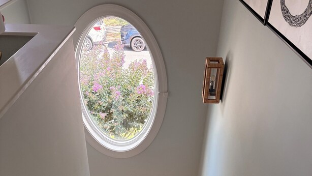 Eine Treppe mit Holzdielen und Teppich, die zu einem Raum mit einem Rundfenster mit Blick auf einen Garten führt.