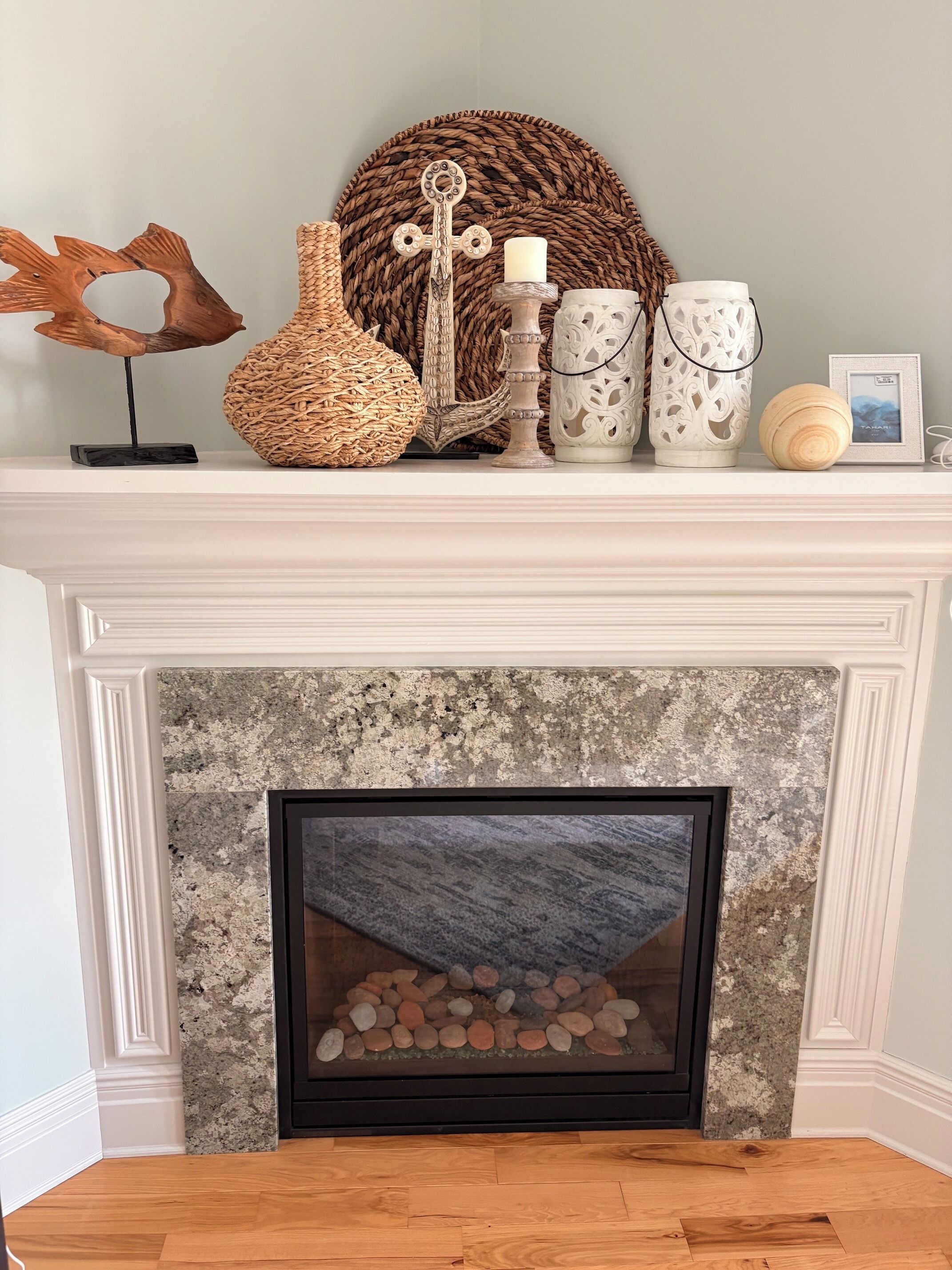 A fireplace with a stone mantle, a framed picture, and decorative items including a woven basket, a candle holder, and two white ceramic vases.