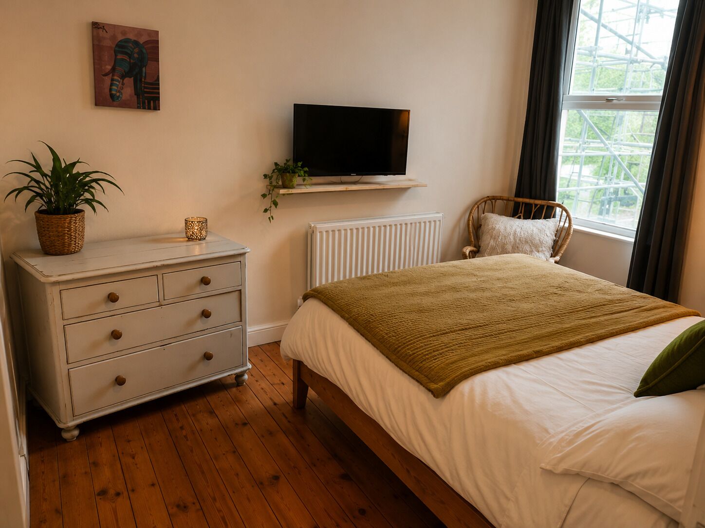 A bedroom with a bed, a dresser, a television, a window, and a plant.
