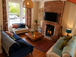 A cozy living room with a brick fireplace, a flat-screen TV mounted above it, and comfortable seating including a sofa and a couch.