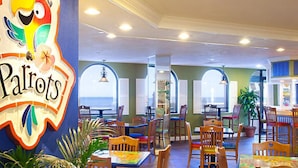 A restaurant interior with wooden tables and chairs, a colorful mural, and large windows.