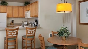A compact kitchen with wooden cabinets, a microwave, a coffee maker, and a dining table with chairs.