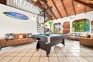 Ein Billardtisch in einem Raum mit hoher Decke, einer Couch und einer Wand mit Wandgemälde.