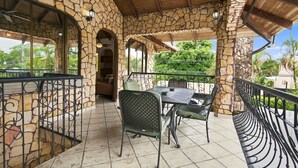 A covered outdoor patio with stone walls, a table with chairs, and a view of greenery. - 11 beds, 9 bdrm, 6 bath - Short walk to Bars, Cocal Casino & Beach (Jacó)
