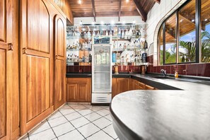 A bar area with wooden cabinets and a large refrigerator stocked with bottles. - 11 beds, 9 bdrm, 6 bath - Short walk to Bars, Cocal Casino & Beach (Jacó)