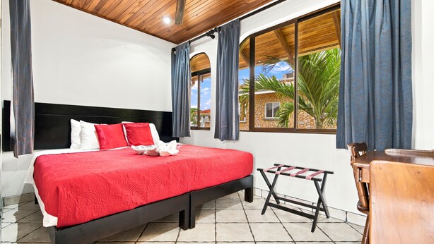 A bedroom with a bed, a window with curtains, a small table, and a chair. - 11 beds, 9 bdrm, 6 bath - Short walk to Bars, Cocal Casino & Beach (Jacó)