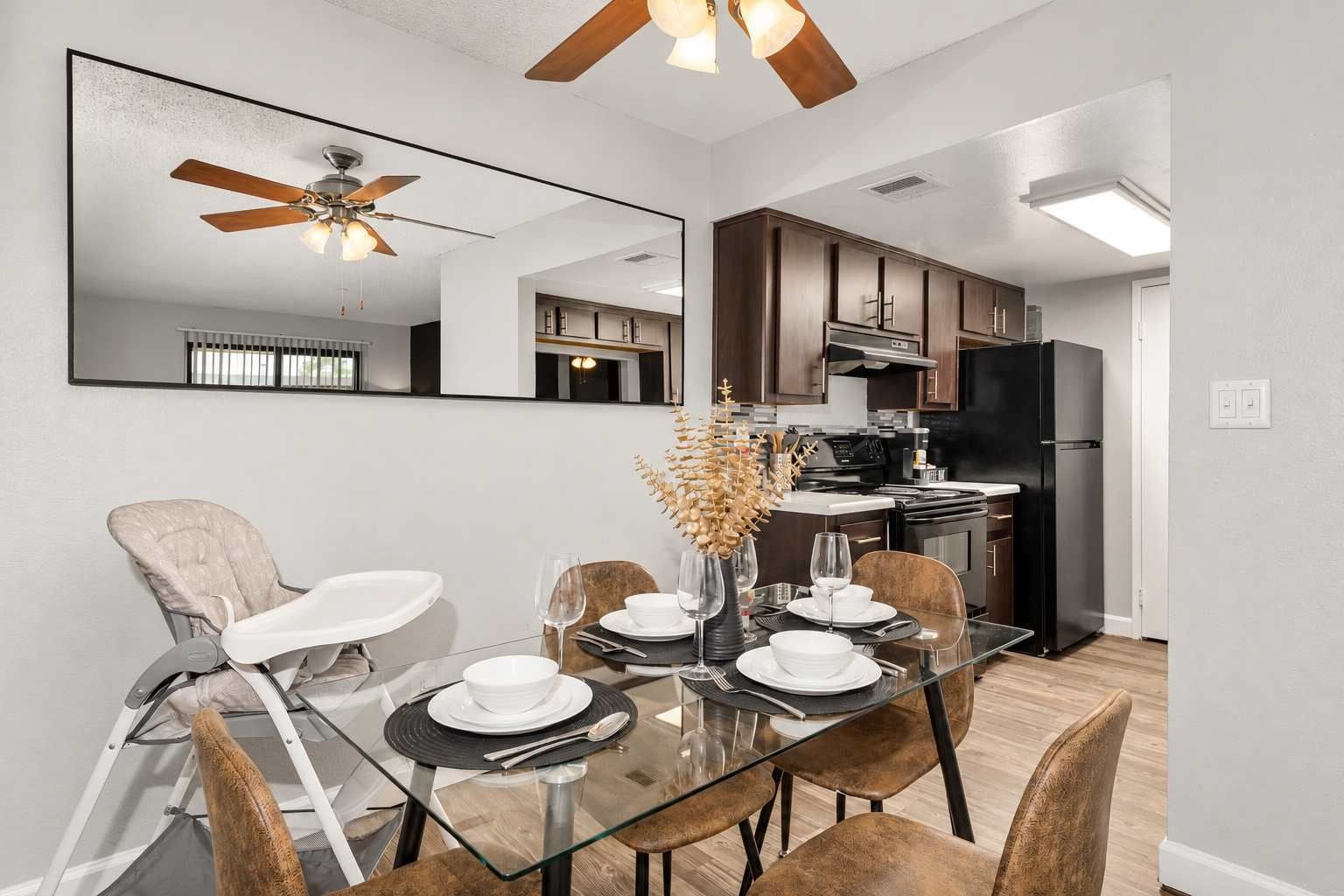 A modern kitchen with dark cabinetry, a black refrigerator, and a dining area with a glass table and chairs.
