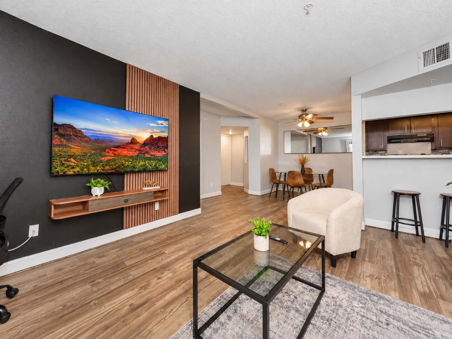 A modern living room with a flat-screen TV, a glass coffee table, and a beige sofa.