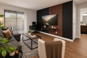 Ein modernes Wohnzimmer mit einer Couch, einem Couchtisch und einem an der Wand montierten Fernseher, versehen mit einem Landschaftsbild.